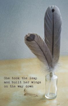 a feather sitting in a glass bottle with a quote on the bottom that reads she took the leap and built her wings on the way down