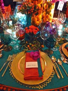 a place setting with oranges, blue and pink flowers on the centerpiece is surrounded by silverware