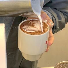 a person pouring milk into a coffee cup with swirly art on the foam in it