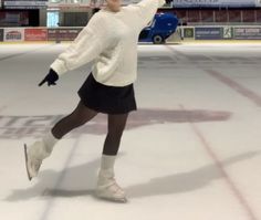 a woman skating on an ice rink in a white sweater and black skirt with her arms outstretched