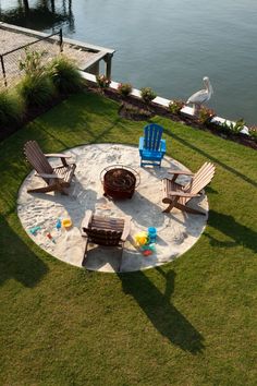 an aerial view of chairs and fire pit in the middle of a grassy area near water