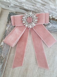 a pink ribbon with a crystal brooch sits on a piece of fabric next to pearls