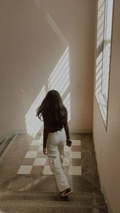 a woman is walking down the stairs in an empty room with sunlight coming through the window