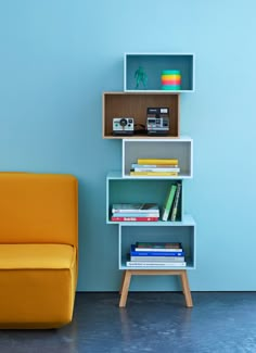 a yellow chair sitting in front of a blue wall next to a bookshelf