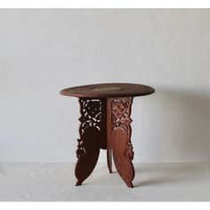 a small wooden table with intricate carvings on the top and bottom, sitting against a white wall