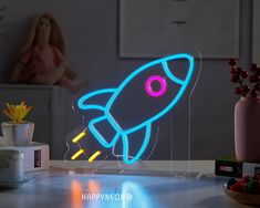 a neon sign with a rocket on it sitting on a table next to a teddy bear