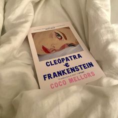 a book is laying on the bed with white sheets and pillows, which are unmade