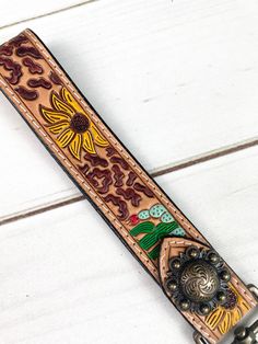 a brown leather belt with flowers and other things on it's side, sitting on a white wooden surface