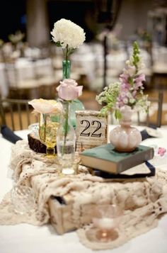 the table is set with flowers, books and vases on top of each other