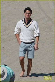 a man in shorts and a sweater walking on the beach