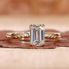 an emerald cut diamond ring on top of a leafy brown surface with gold accents