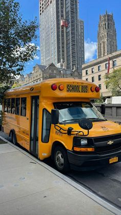 a yellow school bus parked on the side of the road in front of tall buildings