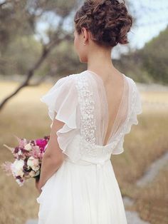 a woman in a wedding dress holding a bouquet and looking at the back of her dress