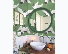 a bathroom with green wallpaper and white birds painted on the walls, including a round mirror