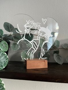 a wooden block holding a glass vase with plants in it on top of a shelf