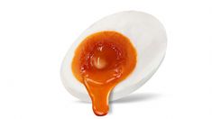 an egg shell filled with orange sauce on a white background, as if it were melted