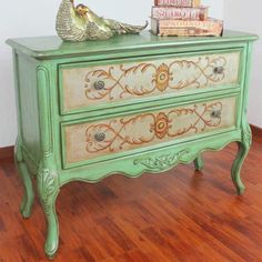 a green painted dresser sitting on top of a hard wood floor next to a stack of books