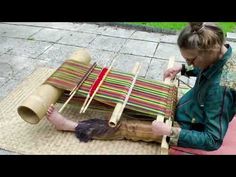 a woman sitting on the ground working on some kind of weaving project with bamboo sticks