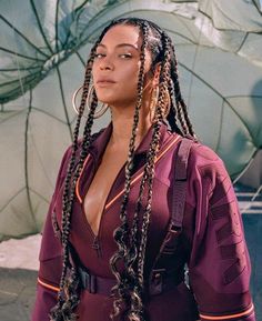 a woman with dreadlocks standing in front of a wall and looking off to the side