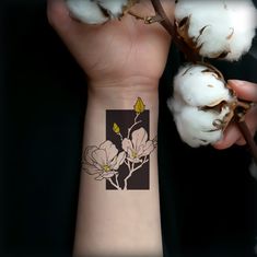 a person with a flower tattoo on their arm next to some cotton flowers and branches