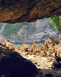 a person sitting on rocks in front of the ocean and some cliffs with trees growing out of them