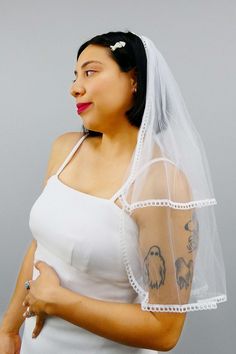 a woman wearing a wedding veil with tattoos on her arm and shoulder is posing for the camera