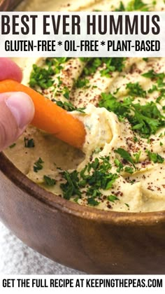 a person dipping hummus into a bowl with carrots and parsley on top