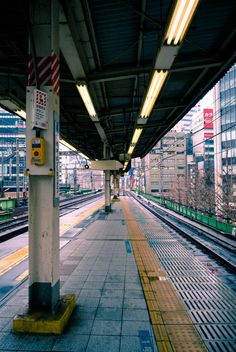 an empty train station with no people on the platform and buildings in the back ground