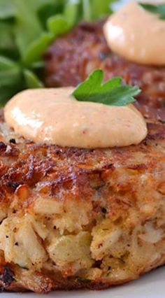 two crab cakes on a white plate with some greens and sauce in the middle, ready to be eaten