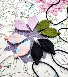 four different colored leaves on a white table cloth with black cords and flowers in the background