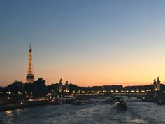 the eiffel tower is lit up in the distance as boats go down the river