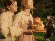 two women in historical dress holding a cake