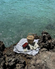 a basket sitting on top of a rock next to the ocean with other items in it