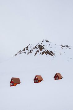 three small red houses in the snow with a mountain in the backgrouund