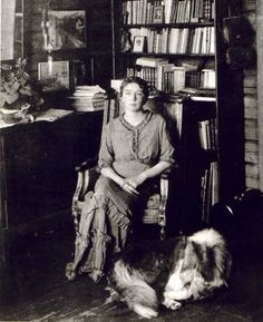 an old black and white photo of a woman sitting in a chair with her dog