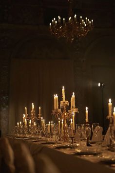 a long table with many candles and wine glasses on it in front of a chandelier