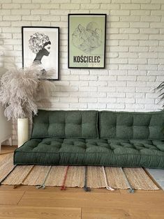 a green couch sitting on top of a wooden floor next to a white brick wall