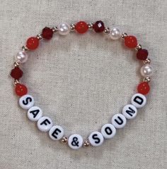 a red and white beaded bracelet that says safe & sound on it with beads