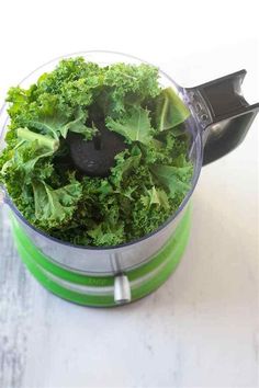 a blender filled with green vegetables on top of a table