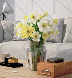 a vase filled with yellow and white flowers sitting on top of a wooden coffee table