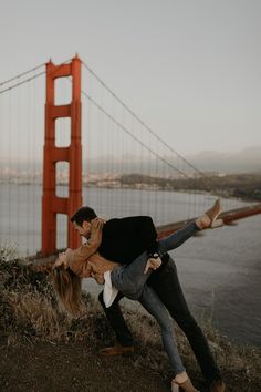 a man and woman are dancing in front of the golden gate bridge with their arms around each other