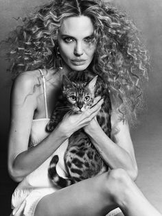 a woman holding a cat in her arms and looking at the camera with an intense look on her face