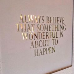 a white wall with gold foil on it and the words always believe that something wonderful is about to happen