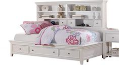 a white bed sitting under a book shelf next to a night stand and nightstand with drawers