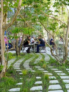 people sitting at tables in the middle of a park with trees and stone walkways