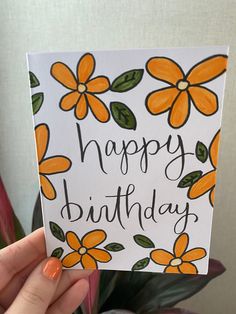 a hand holding up a card with flowers on it that says happy birthday written in black ink