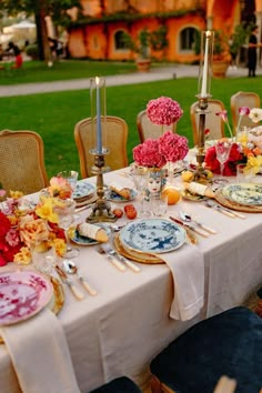 a table set with plates and flowers on it in front of a large lawn area