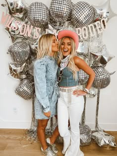 two beautiful women standing next to each other in front of balloons and silver foil letters