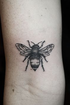 a black and white bee tattoo on the side of a woman's leg,