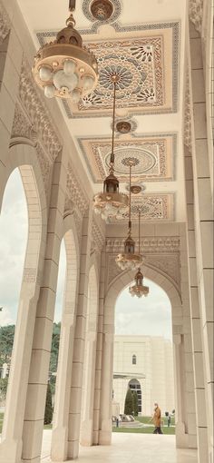 an archway with chandeliers hanging from it's ceiling and two people walking in the distance